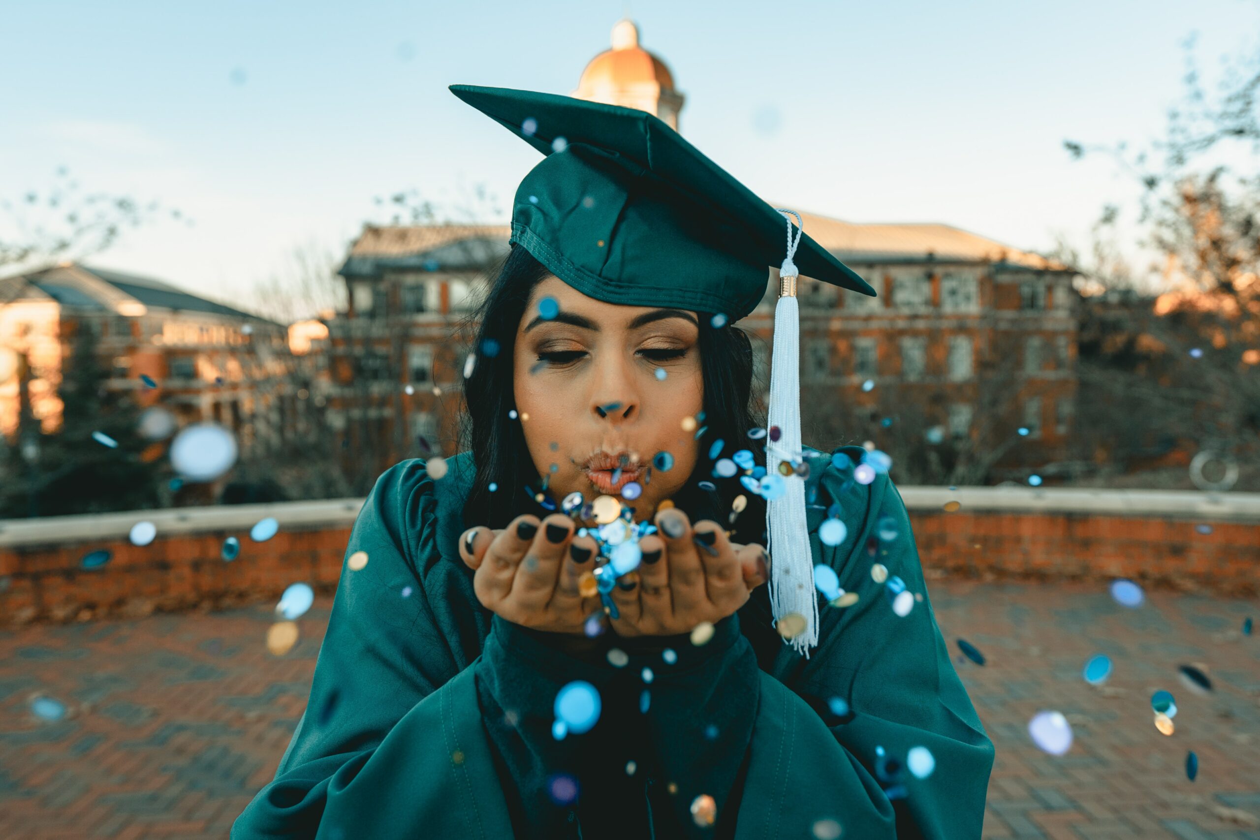 Graduating young woman blowing confetti from her hands